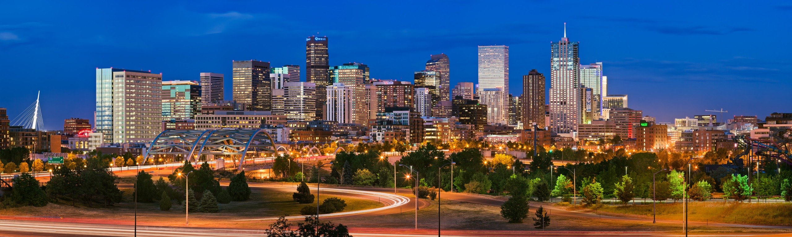 The downtown Denver skyline at dusk, seen from the west with the Speer Boulevard interchange in the foreground